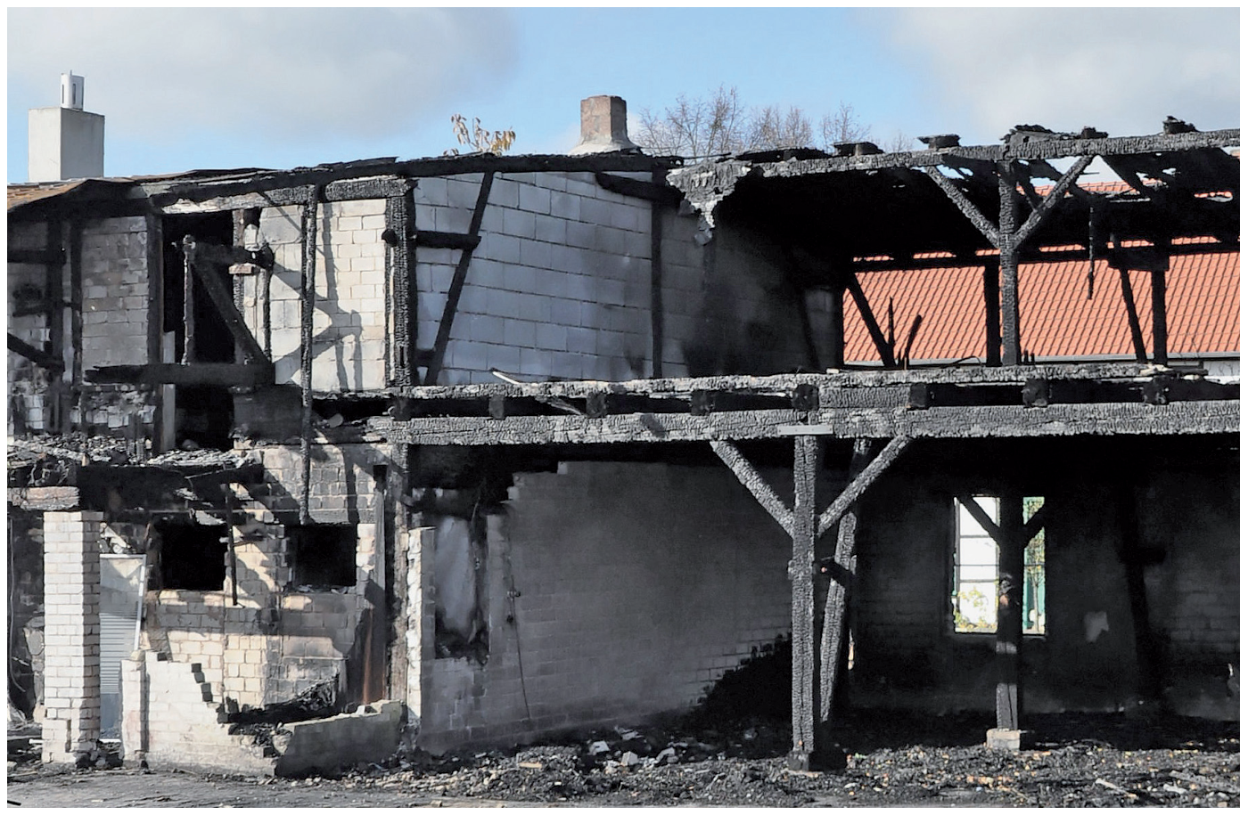 Durch einen Brand verkohlte Holzkonstruktion vor einer unversehrten Kalksand steinwand; wegen ungetrennten Dachanschlüssen wurde das Feuer weitergeleitet
