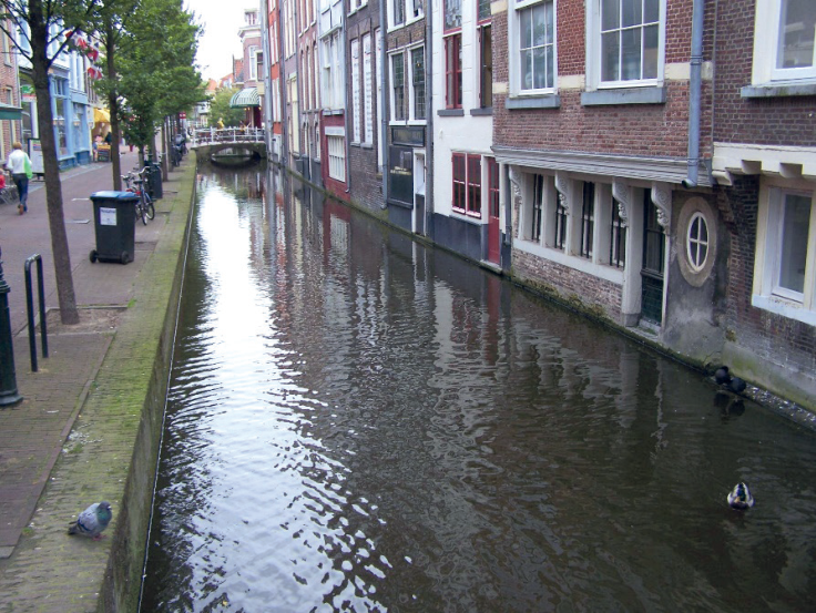 Historische Gebäude an einer Gracht in Delft. Die gemauerten Wände sind nur in Höhe des Wasserspiegels erkennbar nass, unmittelbar darüber aber trocken